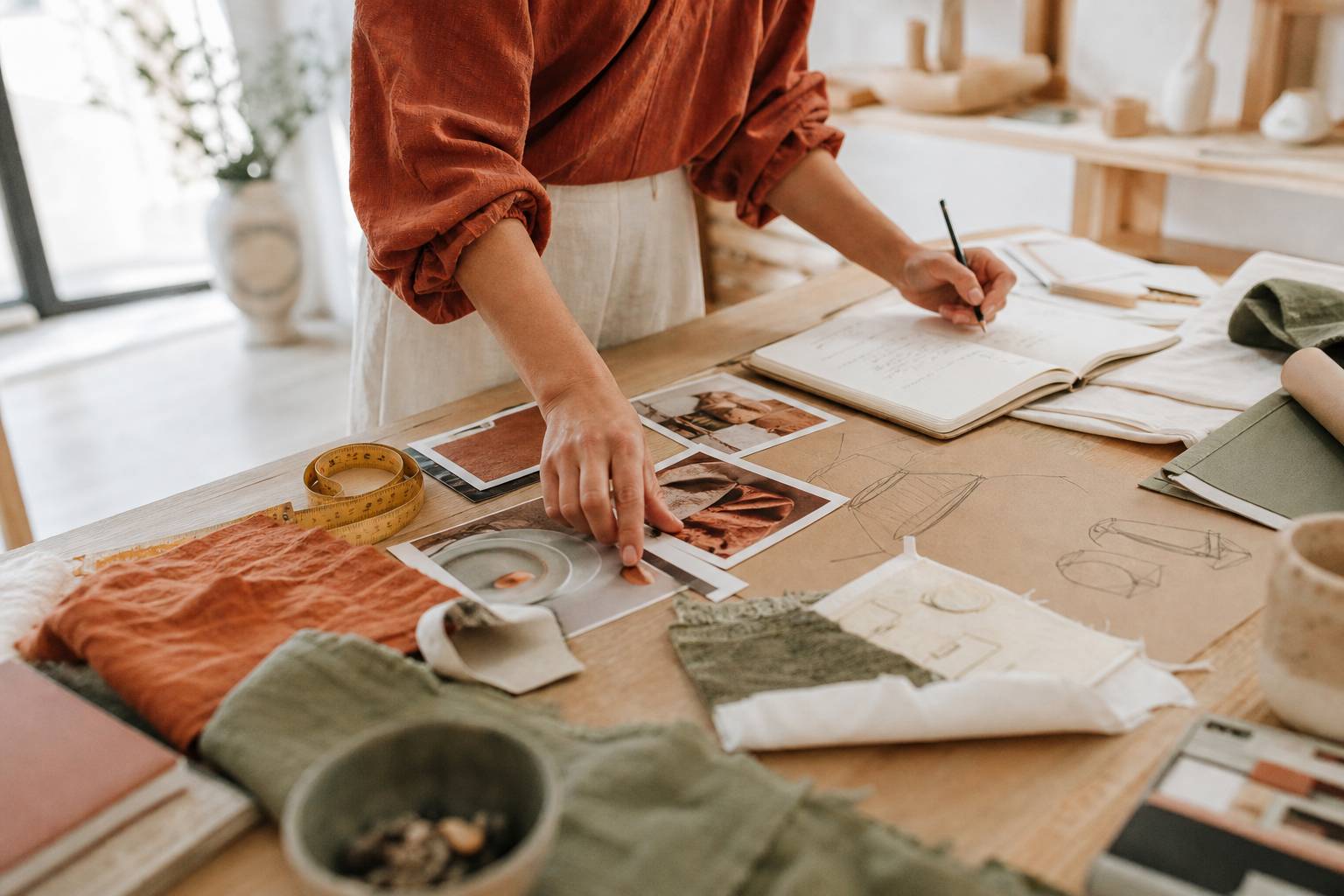 Mains d'artisane documentant ses créations avec photos imprimées et mètre ruban sur table en bois